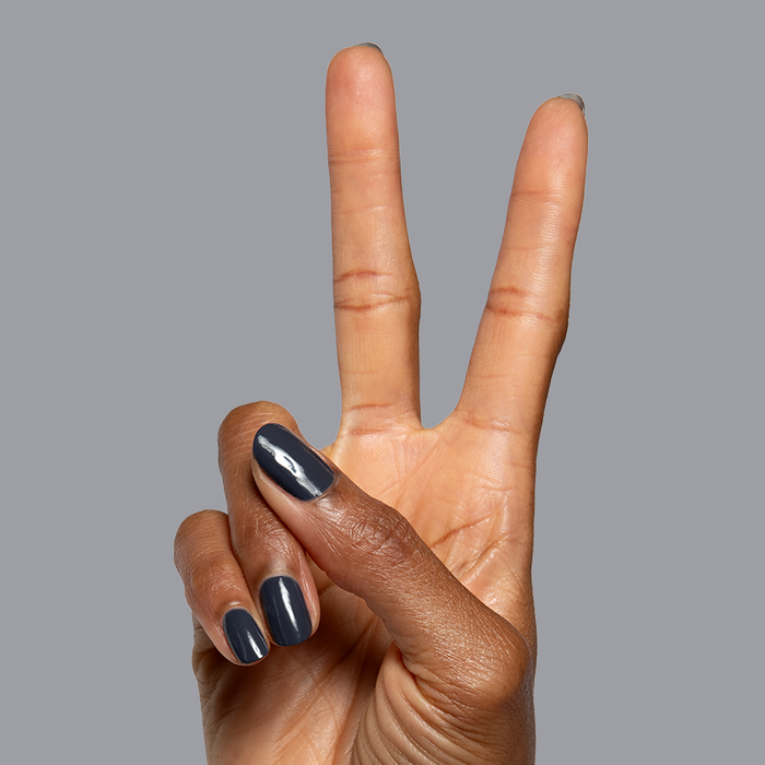 Hand with Inkling deep charcoal gel polish showing a smooth quick dry manicure on a neutral gray background