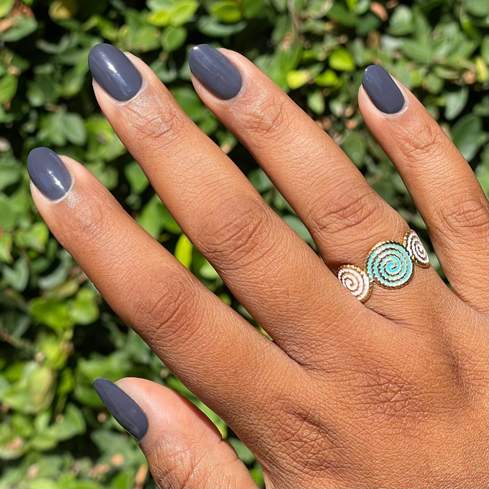 Hand with oval nails painted in Inkling gel polish showing a glossy quick dry manicure outdoors with decorative spiral ring
