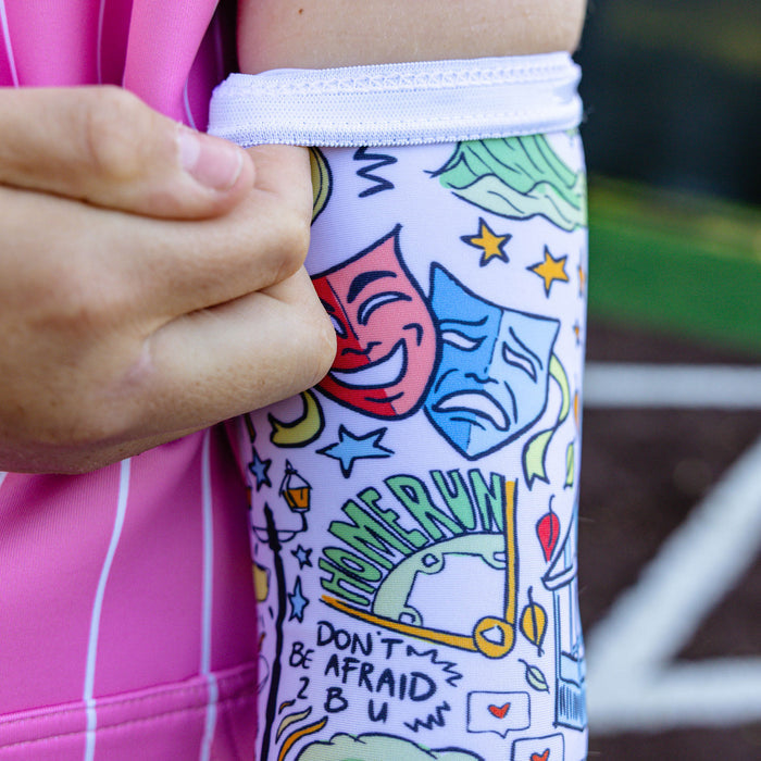 Close-up of the white Jackson Olson x BL101 arm sleeve showing the full all-over illustrated print with theater masks, waves, and BL101 home plate logo