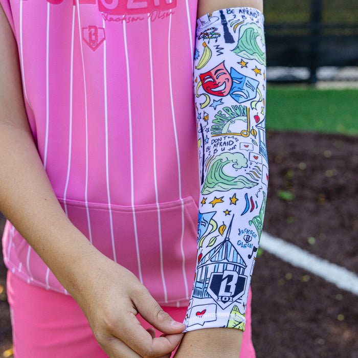 Youth player wearing the white Jackson Olson x BL101 illustrated arm sleeve with the pink pinstripe BSBL-SZN Short Sleeve Hoodie V3