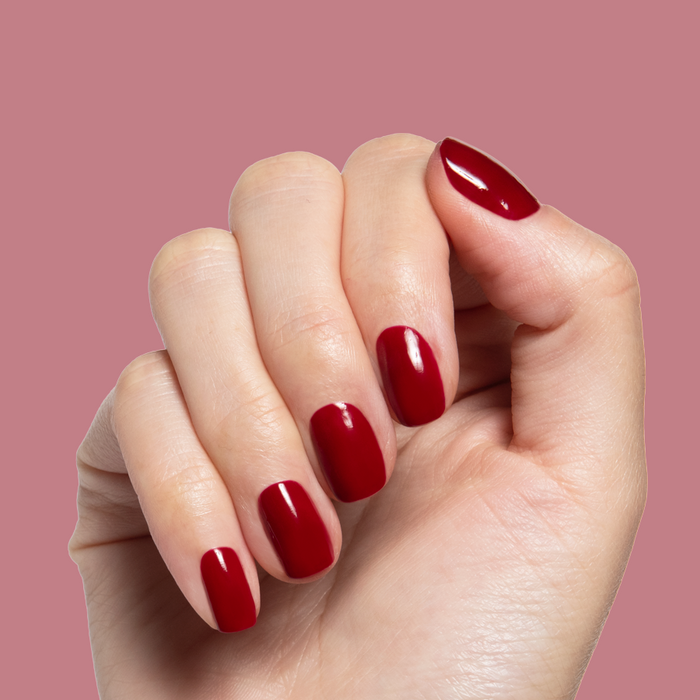 Jammy gel polish on short natural nails with a shiny deep cabernet color against soft pink background