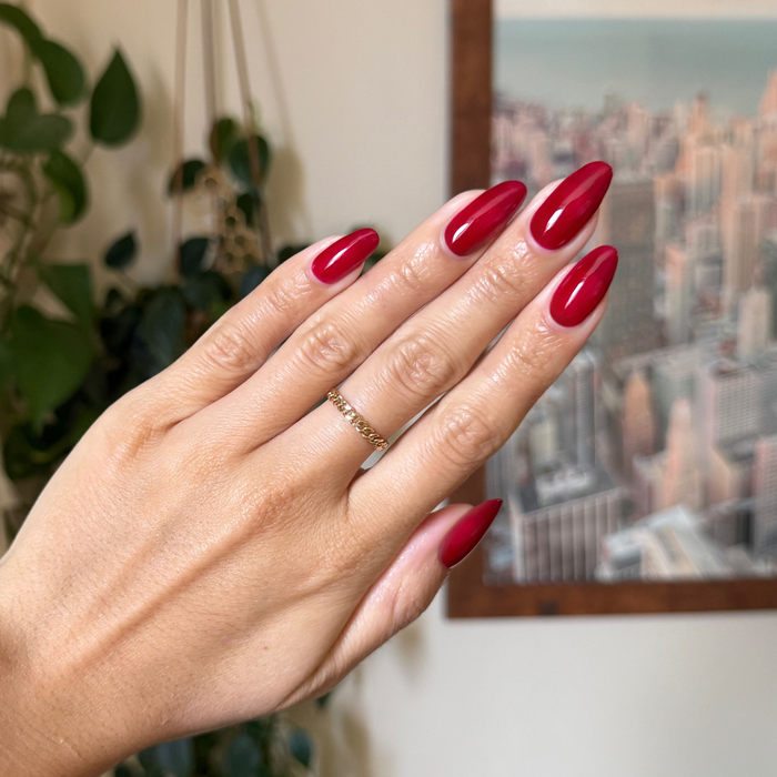Jammy gel polish in vibrant cabernet on almond shaped nails with a smooth glossy finish and subtle gold ring detail