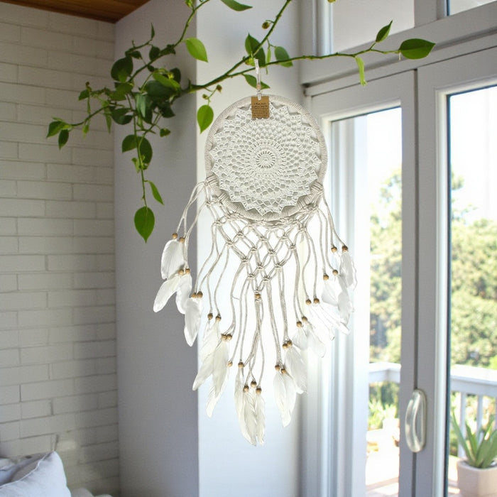 White dreamcatcher with feathers hanging in a room with a window and plant.