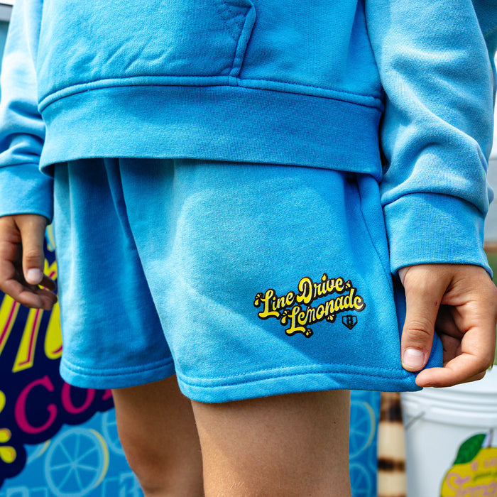 Youth model wearing blue youth shorts with "Lemonade Cup" design