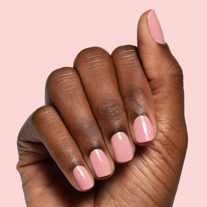 Lovely gel polish in soft dusty rose shade on natural nails with a smooth glossy quick dry finish against pale pink background