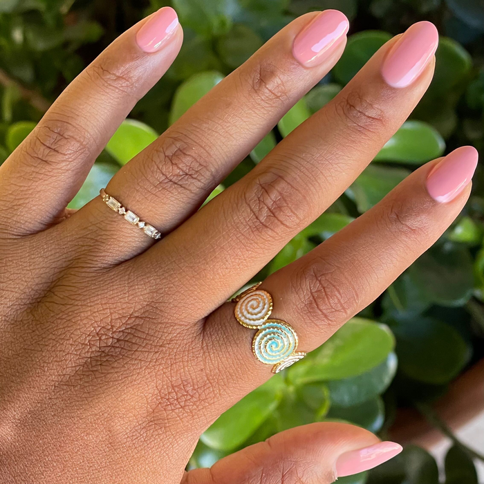 Lovely gel polish on natural nails with a smooth glossy finish shown with delicate gold rings and a green leafy background