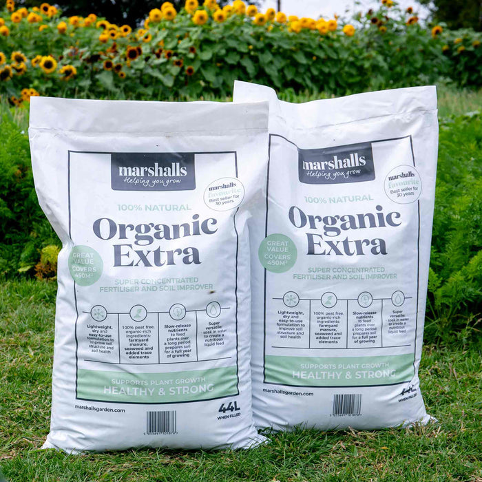 Two bags of Marshalls Organic Extra fertiliser on grass with vegetables and flowers growing in the background.