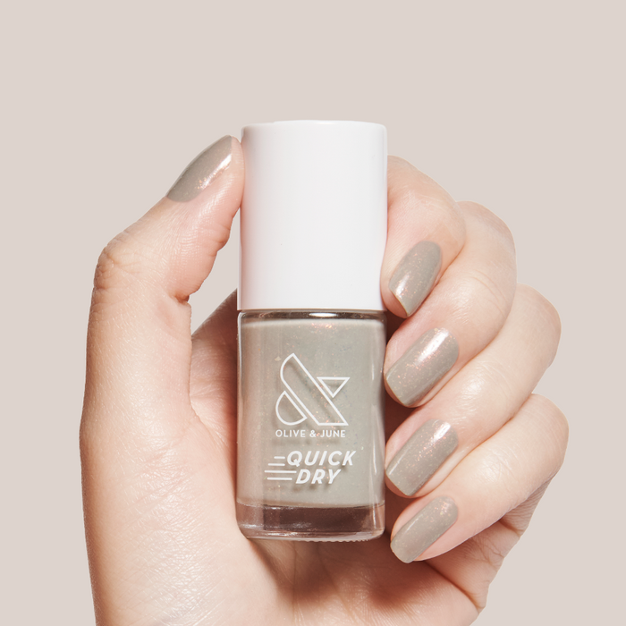 Hand holding Olive and June Moonlit quick dry gel polish bottle with nails in sheer grey holographic manicure