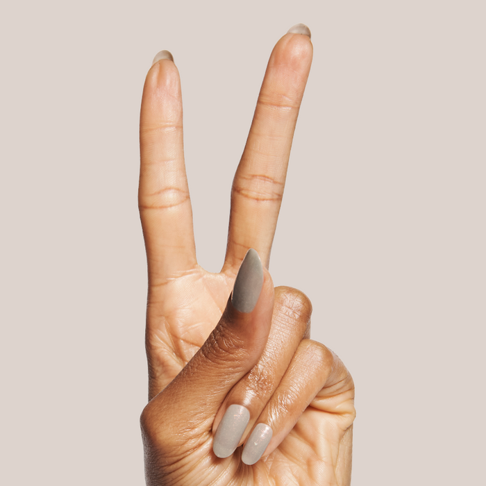 Hand with almond shaped nails in sheer grey Moonlit gel polish holding two fingers up on neutral background