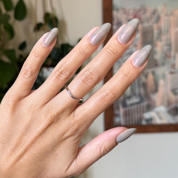 Hand with almond shaped nails painted in Moonlit sheer grey gel polish with holographic flakes over natural skin tone