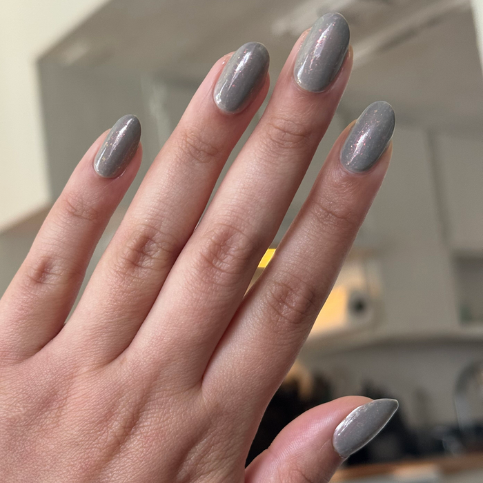 Hand showing nails painted with Moonlit quick dry gel polish in milky grey with holographic shimmer over natural skin tone
