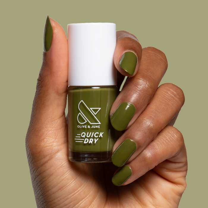 Hand holding Olive and June Mossy quick dry gel polish bottle with matching smooth green manicure on natural nails