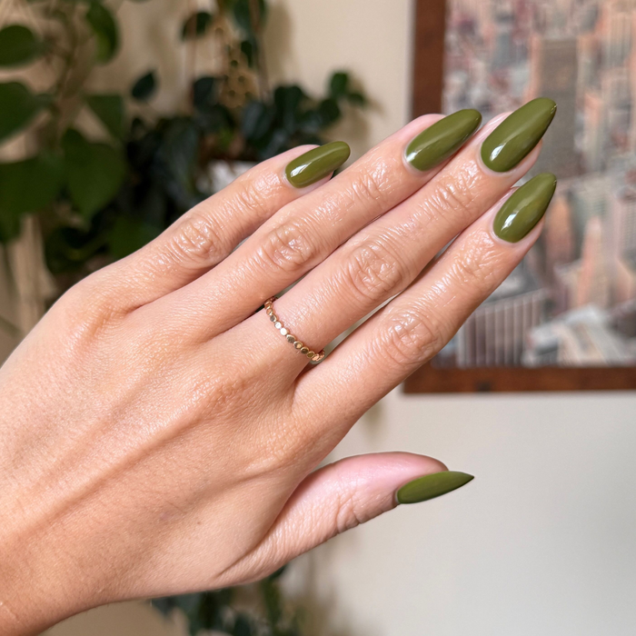 Hand with long nails painted in Mossy gel polish showing glossy quick dry manicure with delicate gold ring