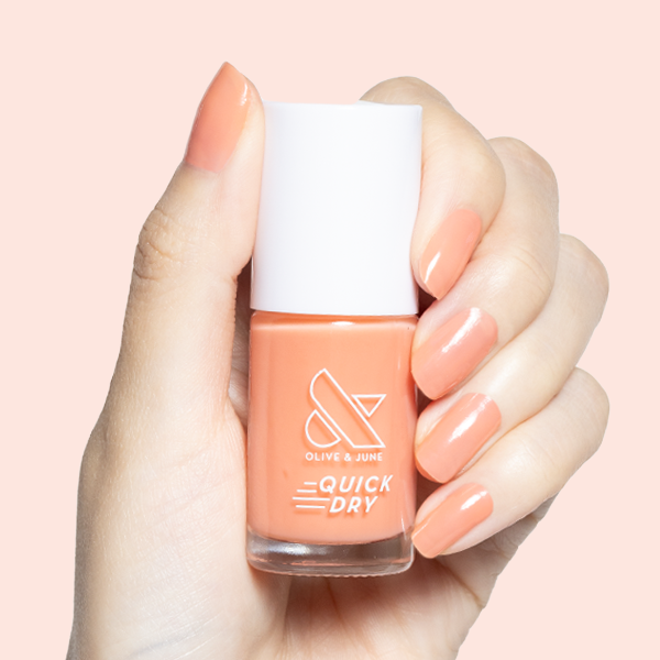Hand holding Peeptoe quick dry polish bottle with matching sheer warm peach glossy manicure on short nails