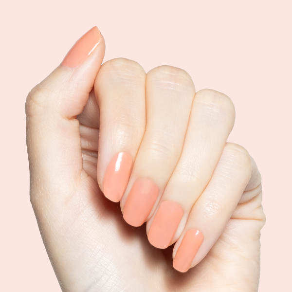 Hand with Peeptoe sheer warm peach polish in glossy finish on medium-length natural nails against pale pink background