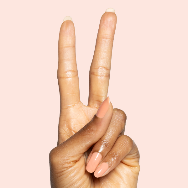 Hand showing peace sign with Peeptoe sheer warm peach glossy manicure on medium-length natural nails against pale pink background