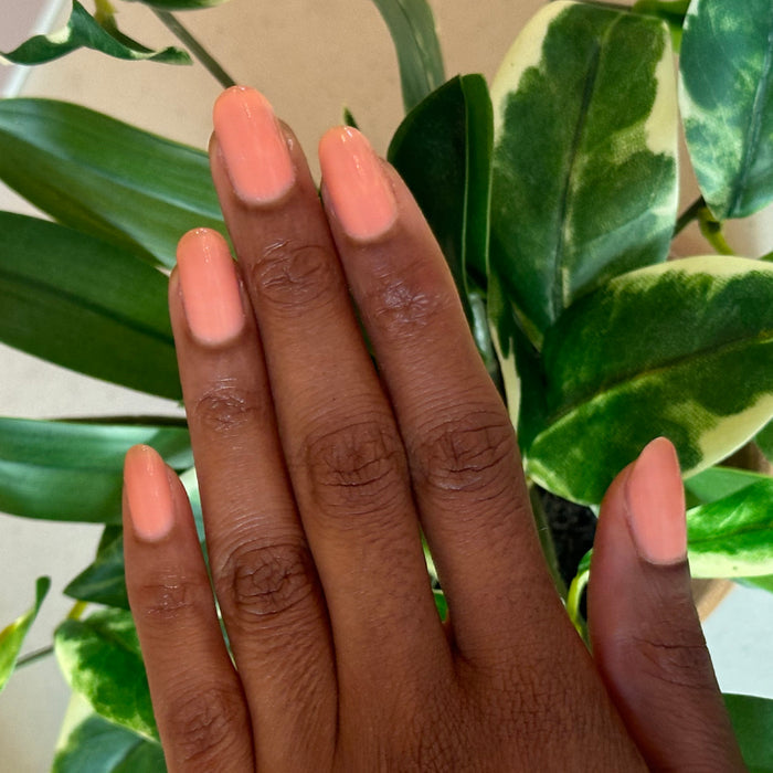 Hand with Peeptoe sheer warm peach gel polish manicure on natural nails over green leafy background