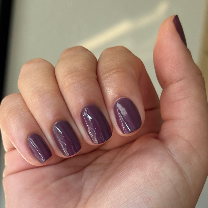 Hand showing glossy Plum gel polish manicure with a rich dark warm purple finish in natural light