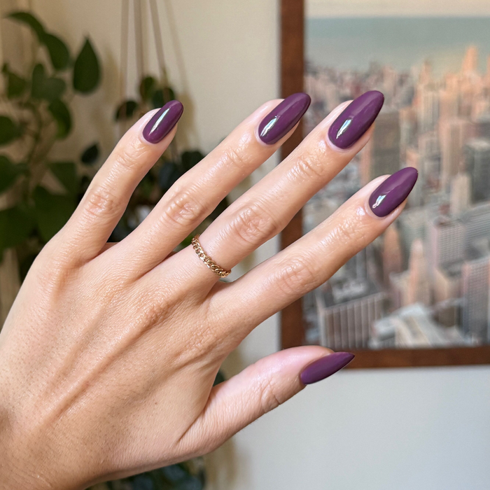 Hand with almond shaped nails in glossy Plum gel polish showing a neat quick dry manicure indoors