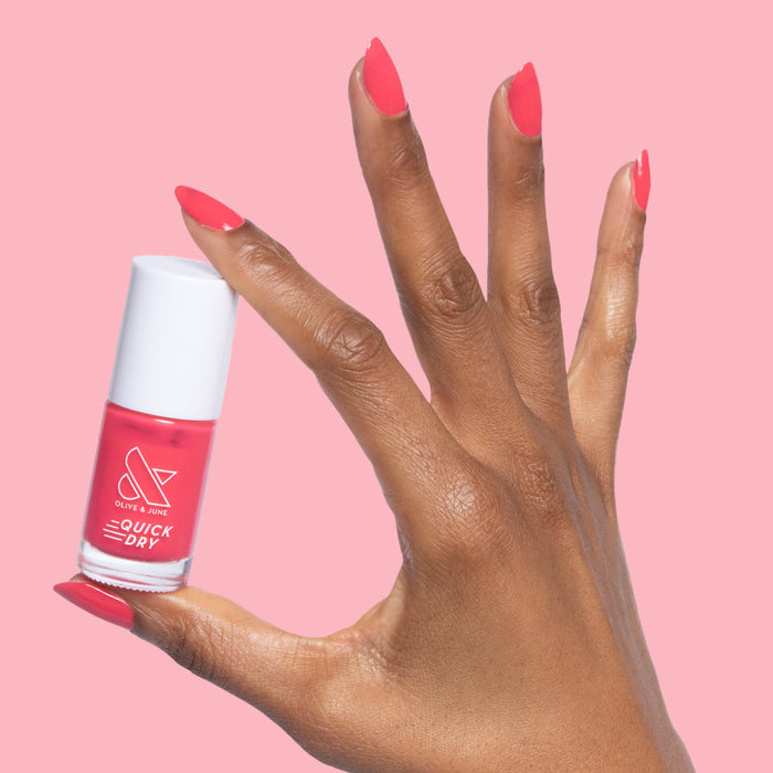 Hand with Pomodoro quick dry nail polish bottle and matching vibrant pinky-tomato red manicure on nails