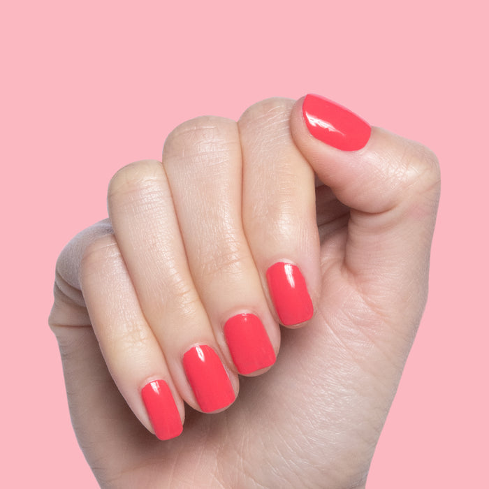 Hand with Pomodoro quick dry polish applied on short natural nails against a soft pink background