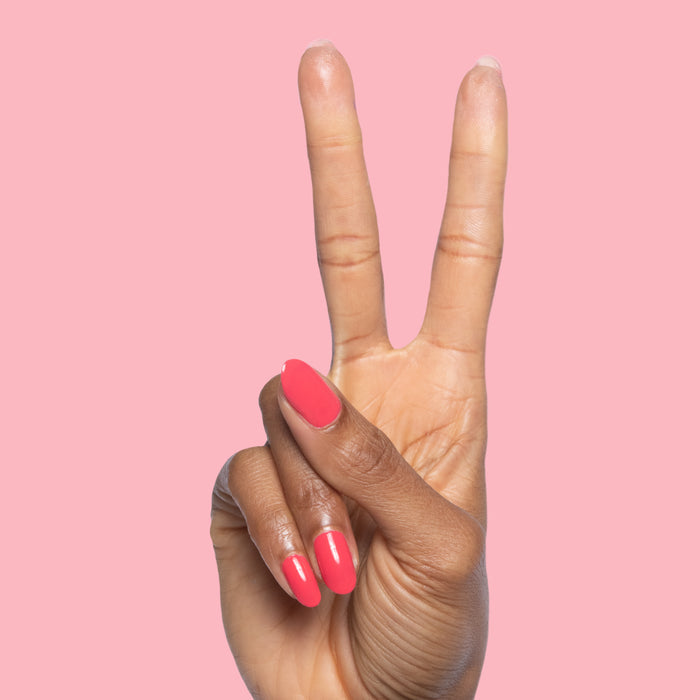 Hand showing two fingers with Pomodoro quick dry polish in pinky-tomato red on smooth short nails against pink background