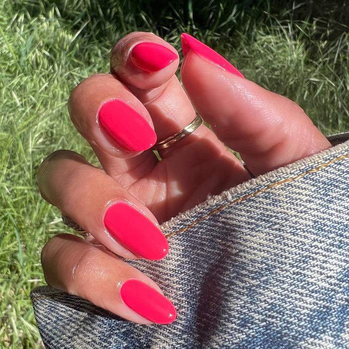 Hand with Pomodoro nail polish in bright pinky-tomato red on natural nails held over denim fabric outdoors