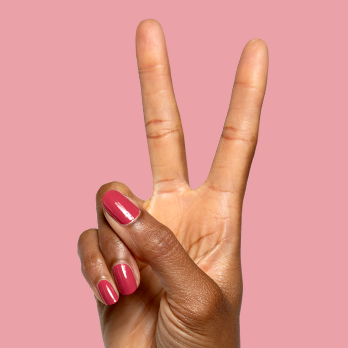 Hand with natural nails painted in glossy Roar quick dry gel polish showing a vibrant mani on soft pink background