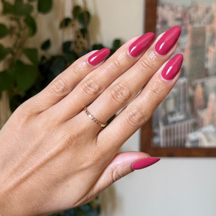 Hand with almond shaped nails painted in glossy Roar gel polish showing a bold, confident manicure indoors