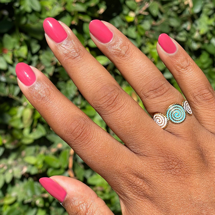 Hand with natural nails painted in vibrant Roar quick dry gel polish outdoors with decorative spiral ring