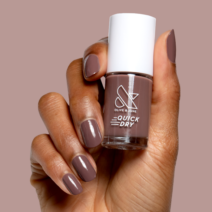 Hand holding Olive and June Sable quick dry gel polish bottle with matching silky brown mani on natural nails