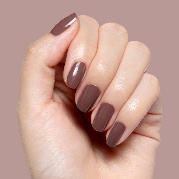 Hand with short natural nails painted in warm Sable gel polish showing smooth quick dry manicure on muted background