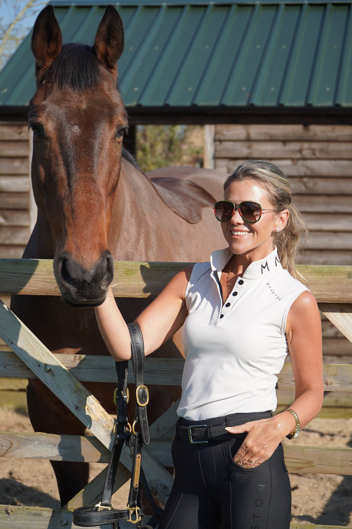 Woman interacting with a horse in an outdoor setting. Ultra-soft technical sport fabric. Breathable and lightweight for warmer weather. Flattering athletic fit
Signature black branded Mayston collar. Subtle gloss shoulder logo detail. Sleeveless design for unrestricted movement. Soft pearl beige colour
