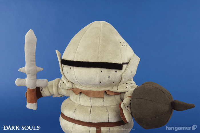 The official Siegmeyer plush photographed against a blue background. It's standing next to its plush sword and shield accessories, which are resting on the ground.