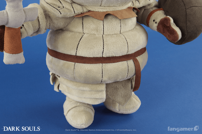 A closeup of the body of the Siegmeyer plush, showing its legs, fabric belt, and multilayer plush armor details, as well as its sword and shield accessories.