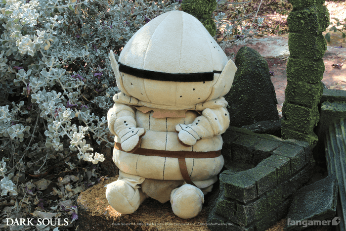 The Siegmeyer plush photographed outdoors, seated next to a flowering bush and miniature ruins.