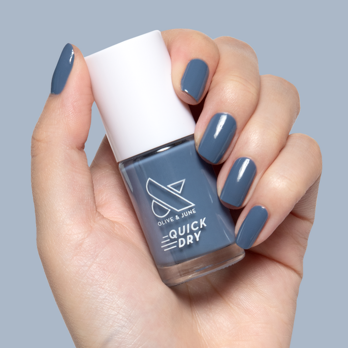 Hand holding Olive and June Slate quick dry gel polish bottle with matching smooth, glossy manicure on square nails