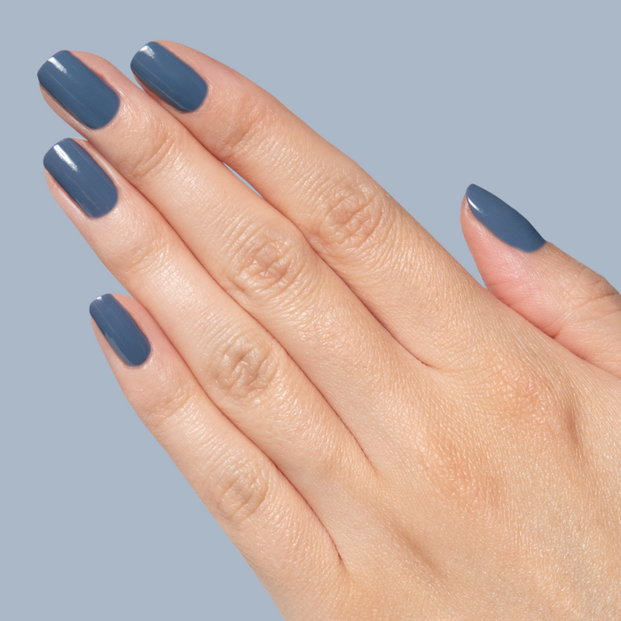 Hand with nails painted in Slate midtone blue gel polish showing smooth glossy quick dry manicure on natural nails