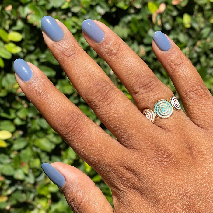 Hand with nails painted in Slate midtone blue gel polish showing glossy quick dry manicure with decorative silver ring