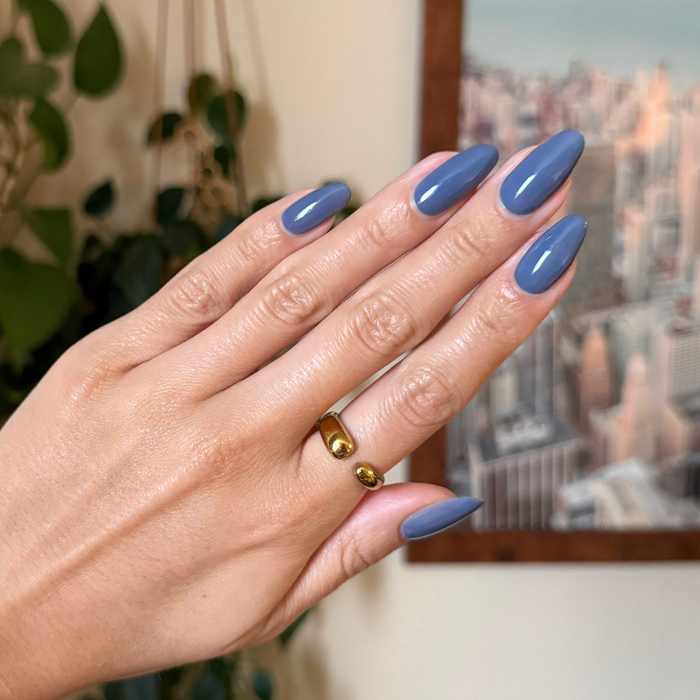 Hand with nails painted in Slate gel polish showing smooth glossy manicure and gold adjustable ring against blurred background