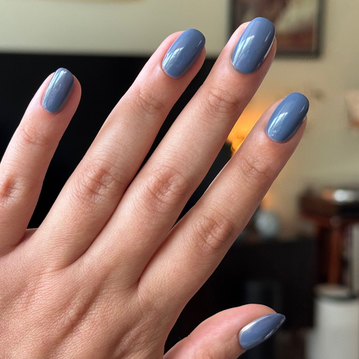 Hand with nails painted in smooth glossy Slate gel polish showing a calm midtone blue mani on natural nails