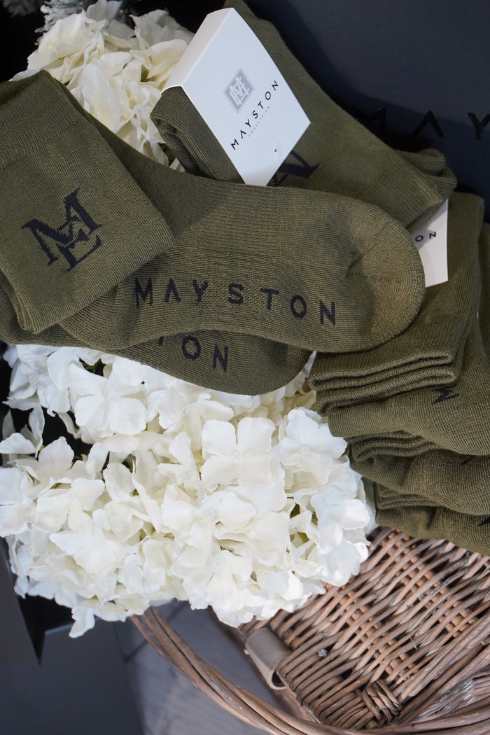 Green socks with 'Mayston' branding on a dark surface with white flowers. thick cotton sock