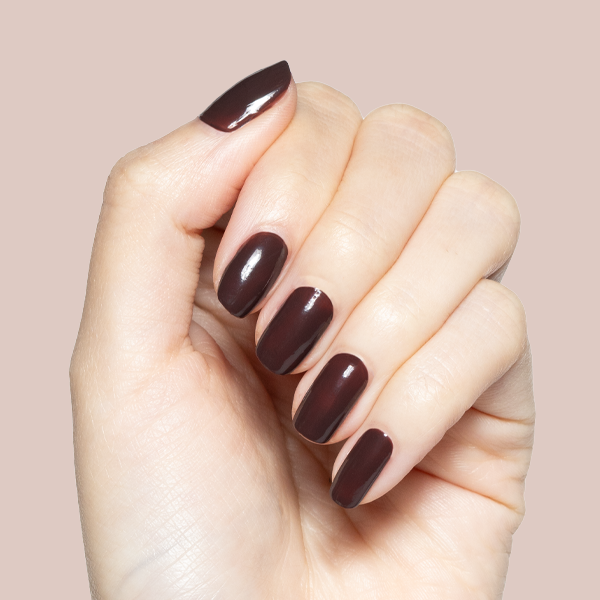 Hand with glossy Spressotini gel polish manicure in dark coffee brown shade on medium-length nails against beige background