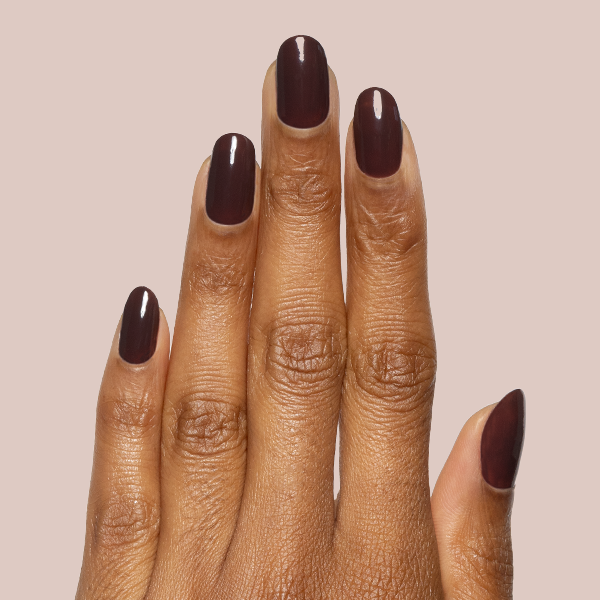 Hand with glossy Spressotini gel polish manicure in rich dark coffee brown shade on medium-length nails against light beige background