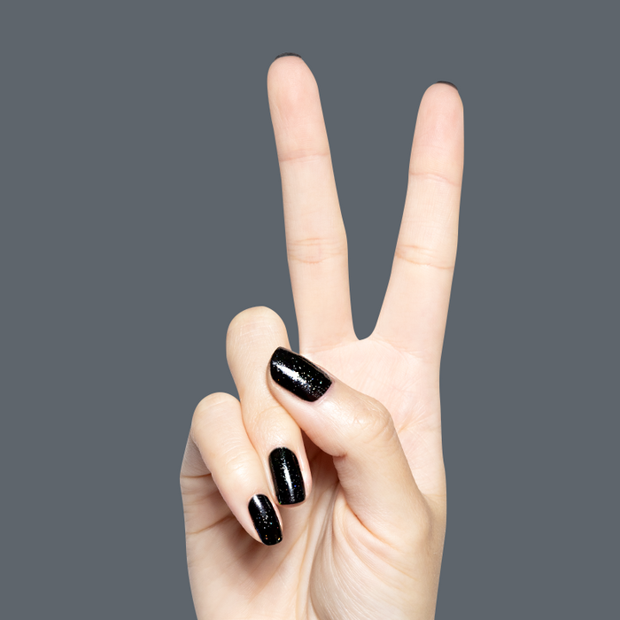 Hand displaying peace sign with glossy black Stargaze gel polish featuring sparkling rainbow glitter on natural nails