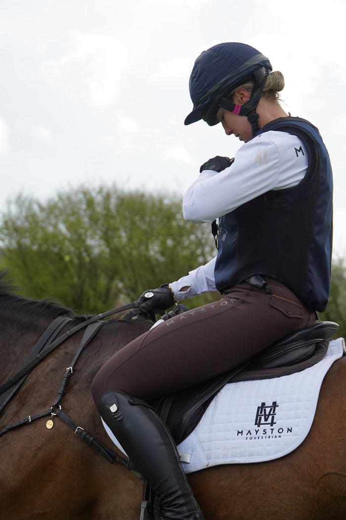 Premium breeches with a Full Silicone seat. Stretch high waisted Jodhpurs. Deep pockets, supportive, comfortable and compression quality fabric. Elegant detailing with subtle branding.  dark brown chocolate. Person cross country training schooling jumping