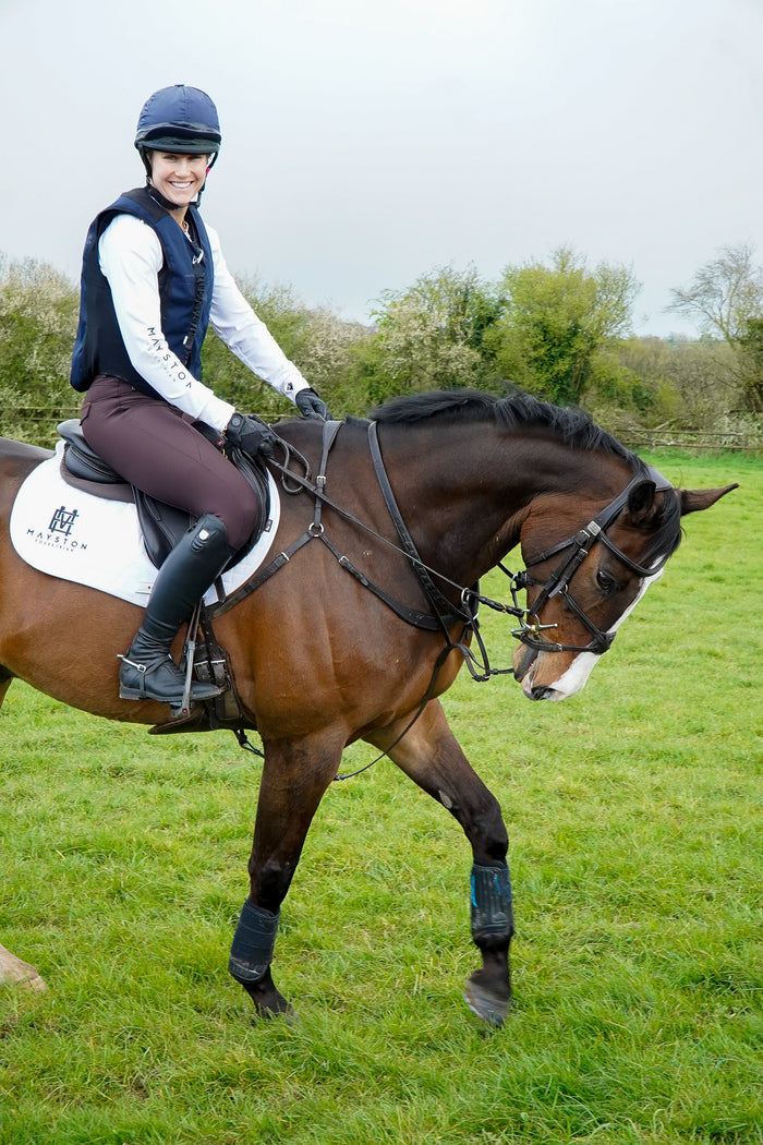 Person riding a horse in a grassy field/ Premium breeches with a Full Silicone seat. Stretch high waisted Jodhpurs. Deep pockets, supportive, comfortable and compression quality fabric. Elegant detailing with subtle branding.  dark brown chocolate