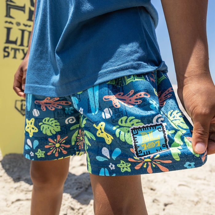 Youth model wearing multi-color youth shorts with "Surfside Slugger" design