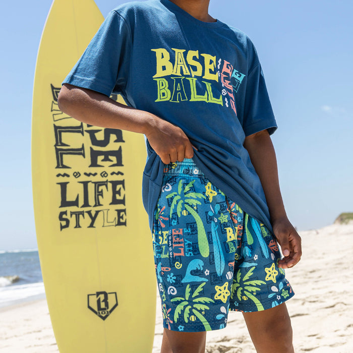 Youth model wearing multi-color youth shorts with "Surfside Slugger" design