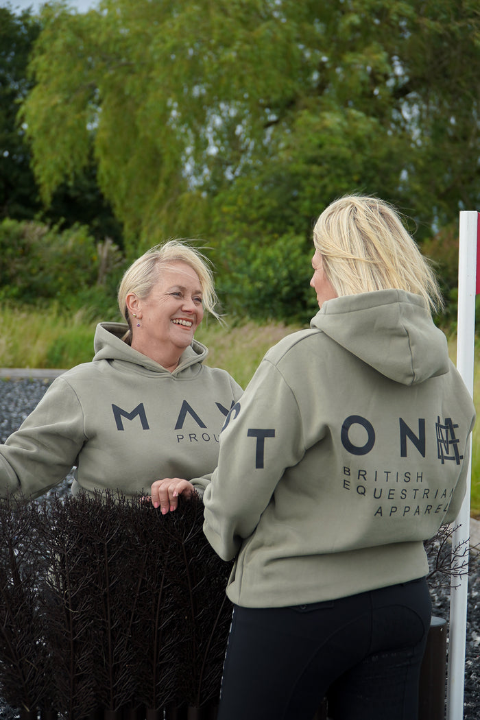 Two women wearing matching green hoodies with branding in an outdoor setting. A person wearing a green hoodie with a large hood, standing next to a white horse. The person is wearing black pants and black boots, and the hoodie has the word 'Equestrian' written on it.
High quality luxurious 100% cotton. wrap around bold logo. soft, cozy and  warm. Hoodie, jumper sweatshirt. everyday wear. casual and smart